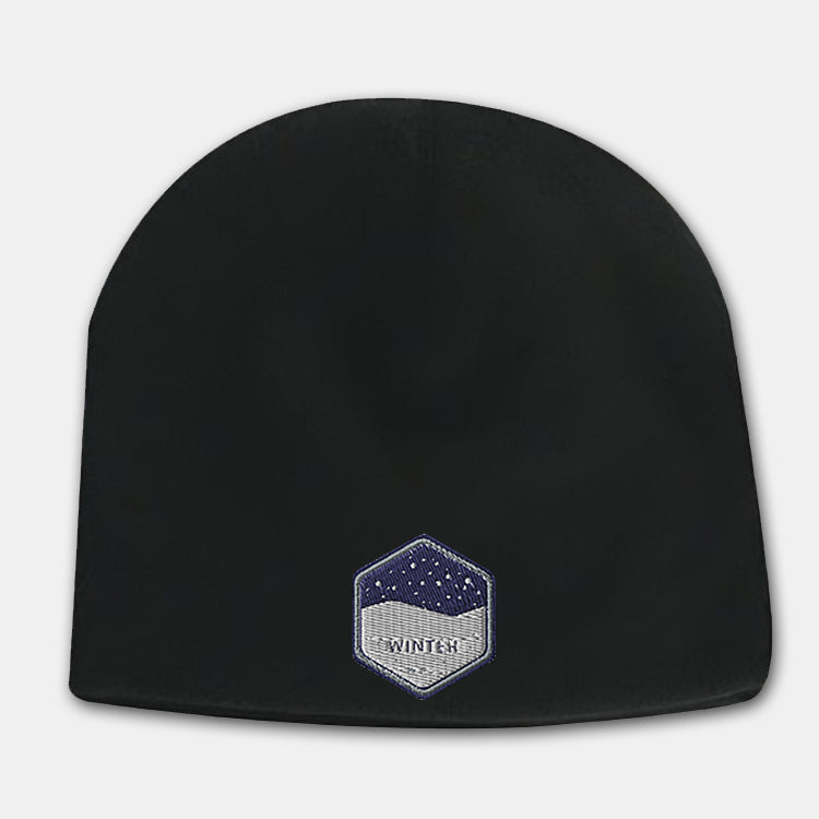Black deluxe fleece beanie with a hexagon-shaped embroidered patch featuring a snowy night design and the word “WINTER” on the front.