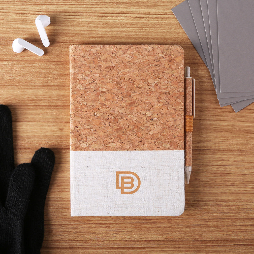 Eco-friendly journal with cork top and beige linen bottom, featuring a minimalist DB logo printed in brown, and a matching cork-covered pen secured in an elastic loop on the right side