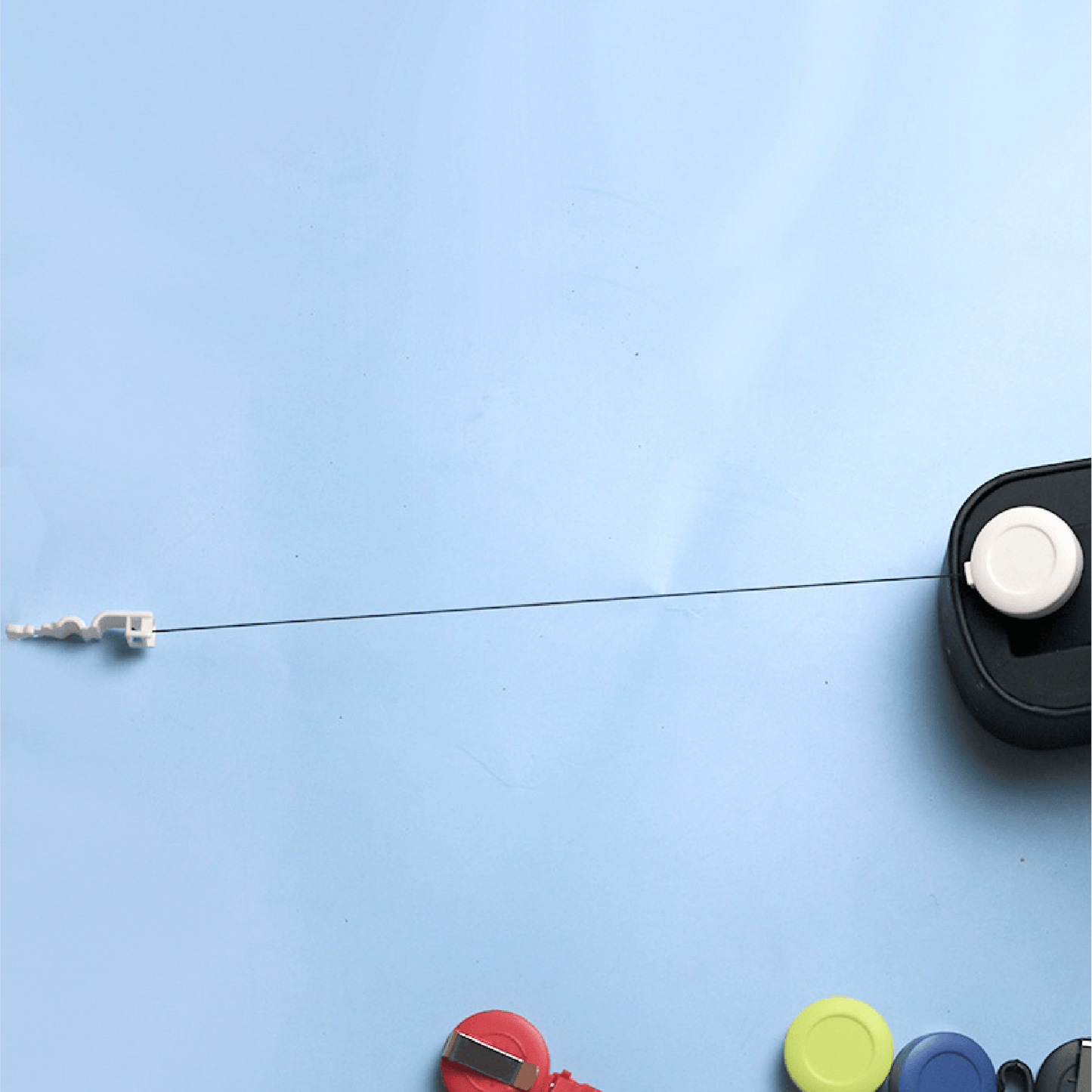 Retractable badge reel with extended nylon cord and white clip end, shown pulled out from a black reel housing against a light blue background.