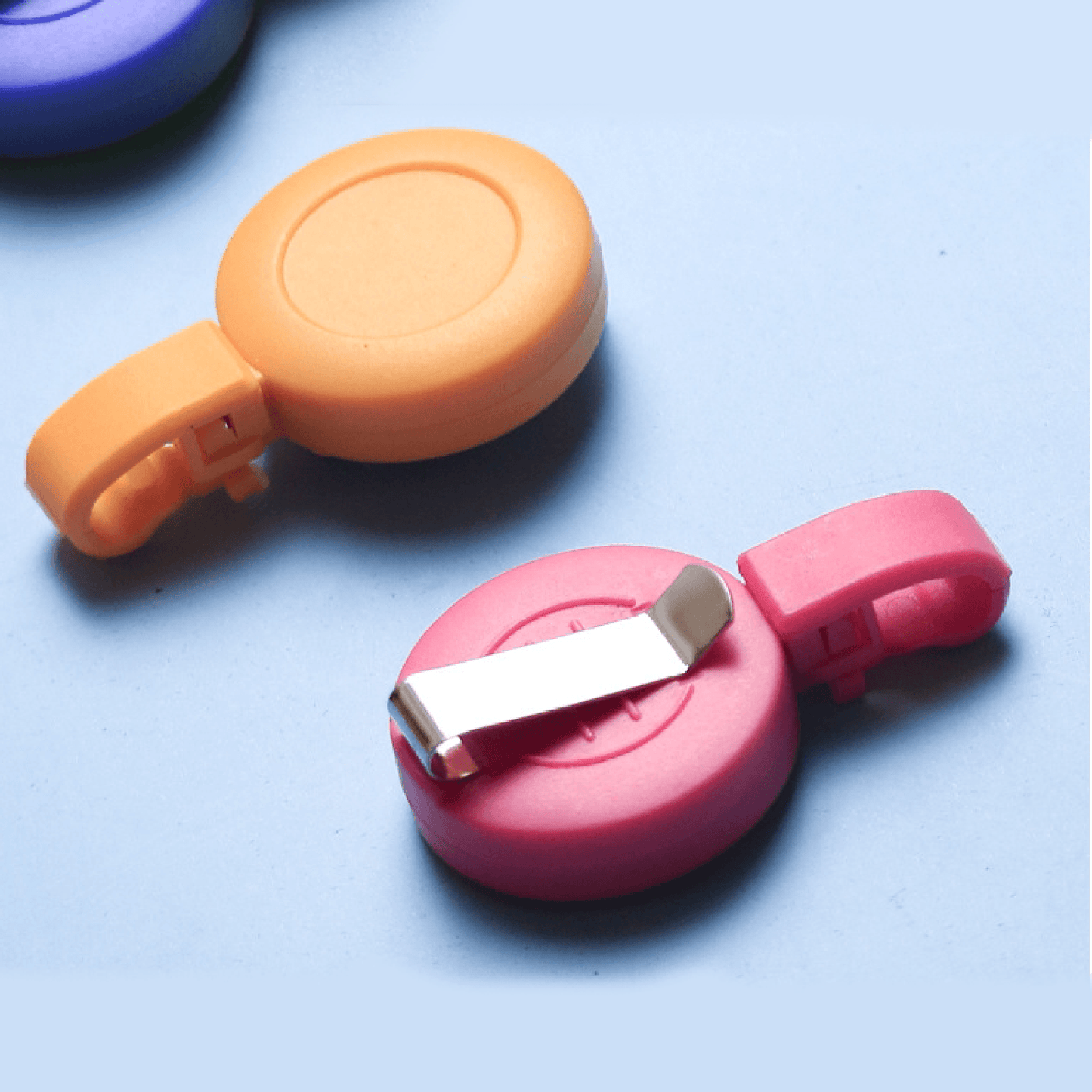 Orange and pink retractable badge reels with metal clips, customizable with your logo, displayed on a light blue background—ideal for ID cards or access badges.