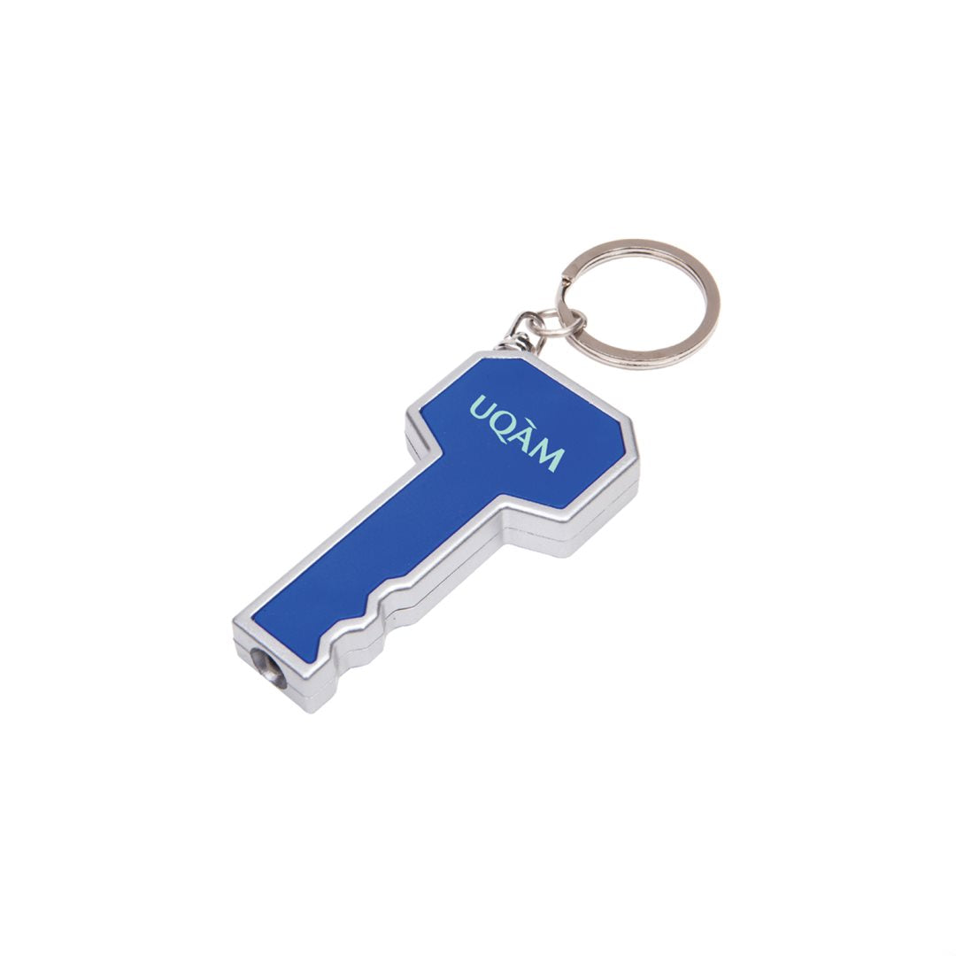 Key-shaped LED flashlight keychain in blue and silver, featuring a customized 'UQÀM' logo printed on the head and a bright white light at the tip; includes attached metal keyring.