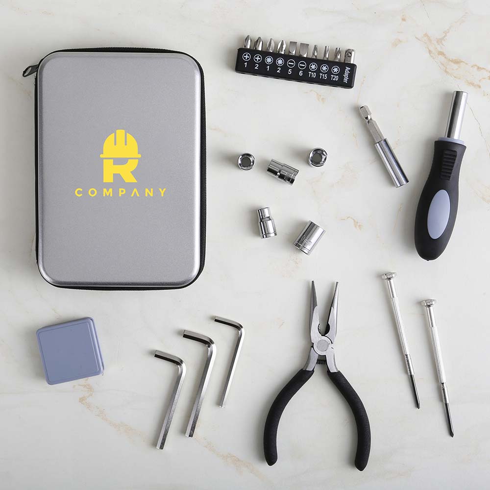 Flat lay of a compact gray tool kit with a yellow logo, surrounded by various tools including pliers, screwdrivers, Allen keys, socket heads, and a bit driver on a marble surface.