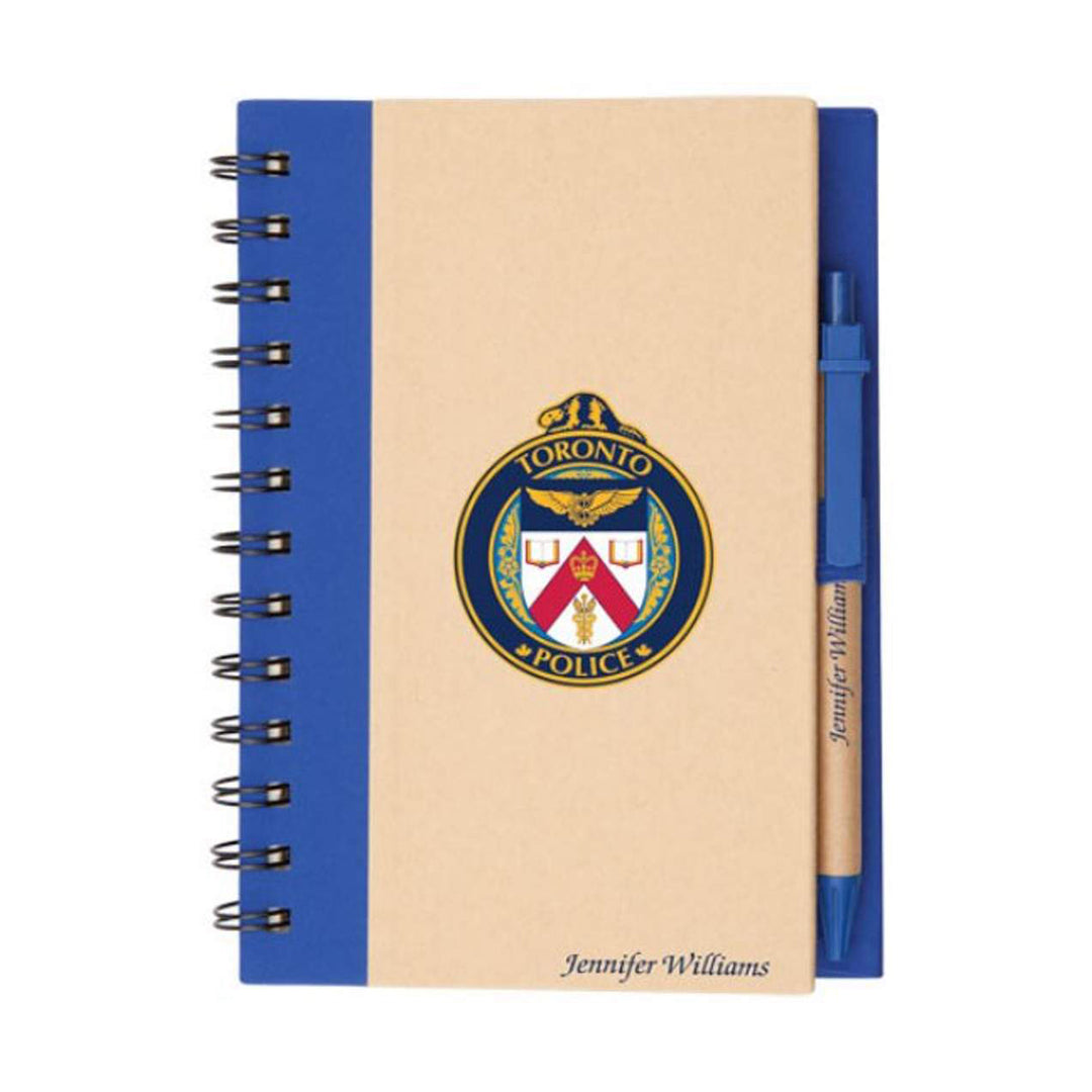 Eco-friendly spiral-bound notebook with a kraft paper cover, black spine, and pen holder on the right side, featuring a matching blue-ink pen and a logo printed on the front.