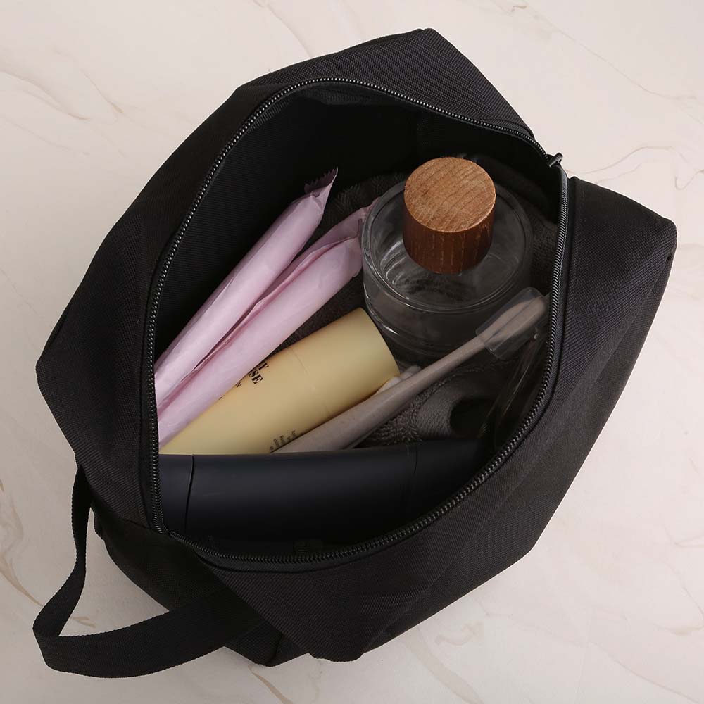 Top-down view of open black toiletry bag filled with personal care items including a toothbrush, bottle, and hygiene products