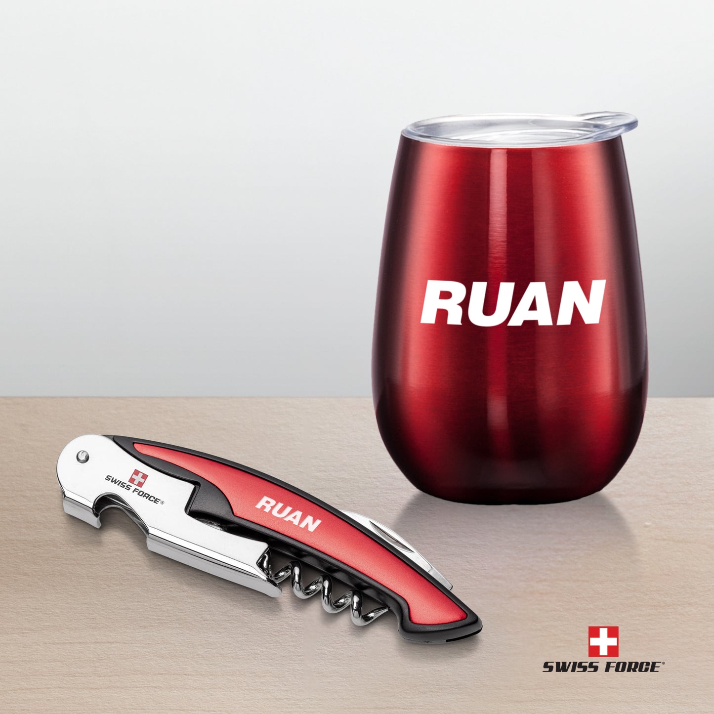 Swiss Force® Rosette Wine Gift Set featuring a red stainless steel wine tumbler with white 'RUAN' branding and a matching red and silver corkscrew with engraved logo, set on a light wood surface