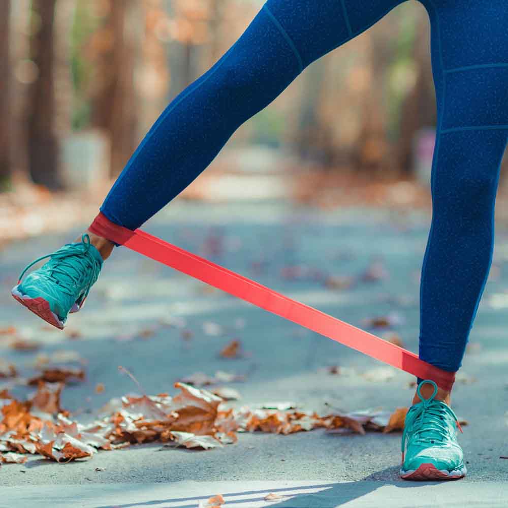 Person exercising outdoors with red resistance band around ankles.