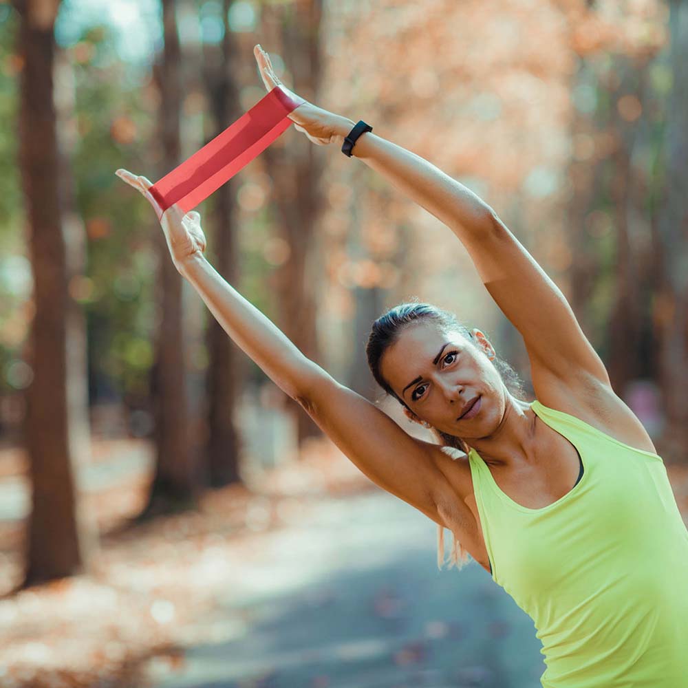 Woman stretching with red resistance band above her head in an outdoor setting