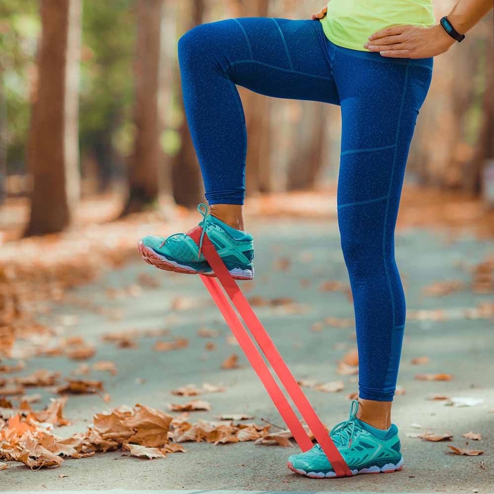 Close-up of a person performing leg resistance band exercise outdoors, wearing blue leggings and teal sneakers