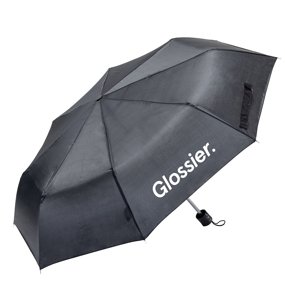 Compact black umbrella with white Glossier logo on canopy panel, curved design, and black handle with wrist strap