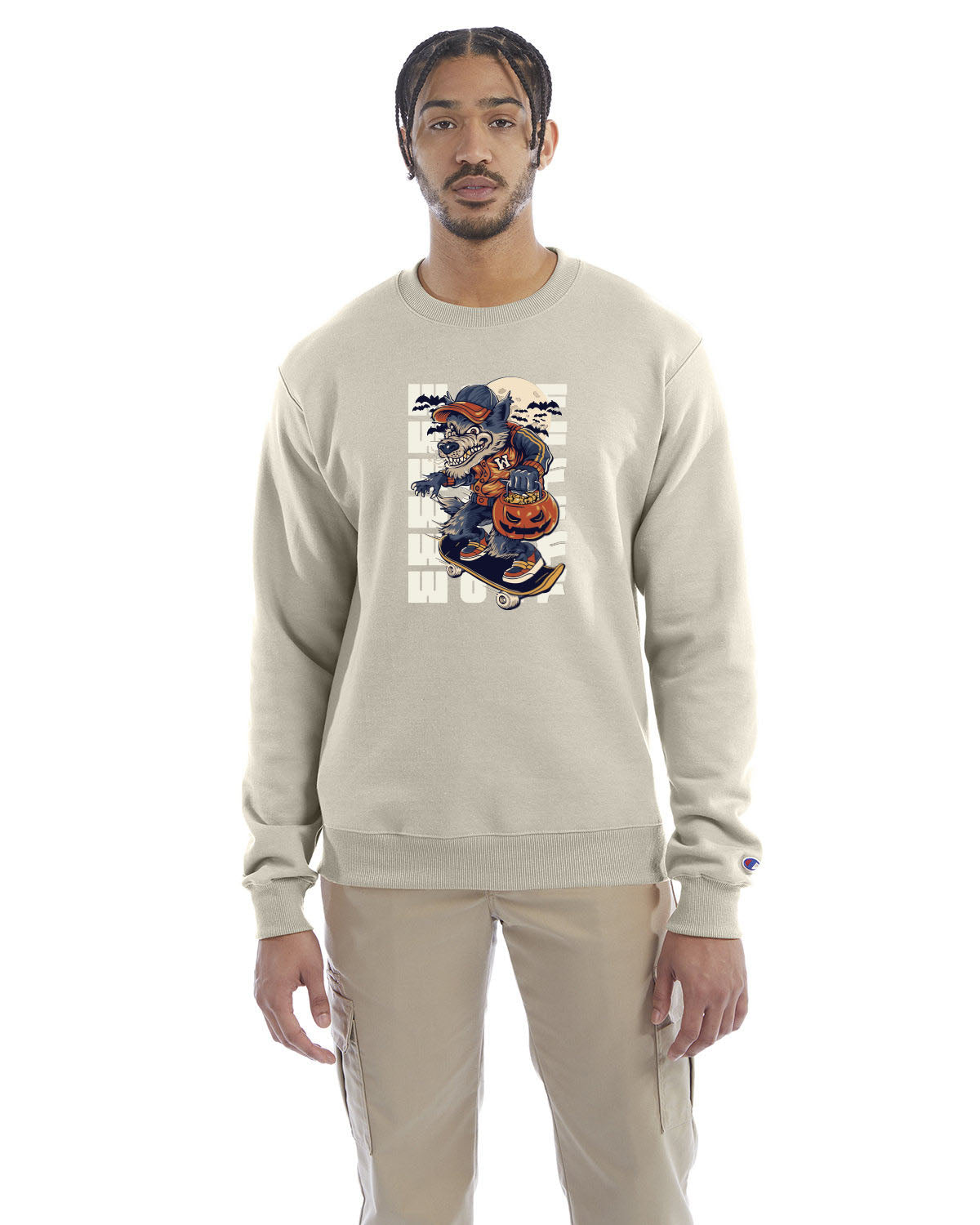 Sand crewneck sweatshirt with a Halloween-themed graphic of a cartoon werewolf skateboarding with a pumpkin basket, worn by a model in beige pants.