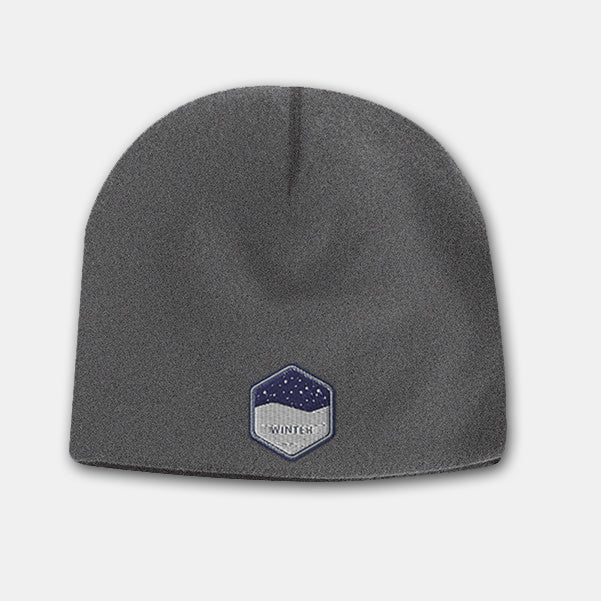 Dark grey deluxe fleece beanie with a hexagon-shaped embroidered patch featuring a snowy night design on the front.