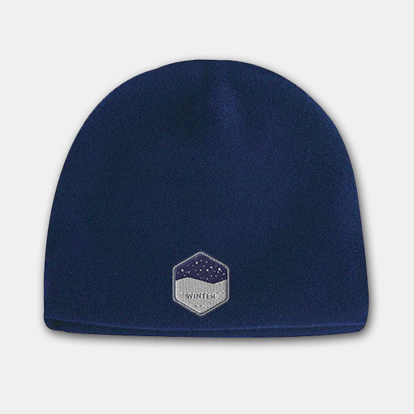 Navy blue deluxe fleece beanie with a hexagon-shaped embroidered patch featuring a snowy night design on the front.