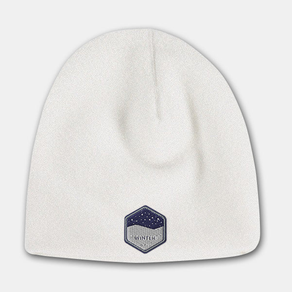 White deluxe fleece beanie with a hexagon-shaped embroidered patch featuring a snowy night design on the front.