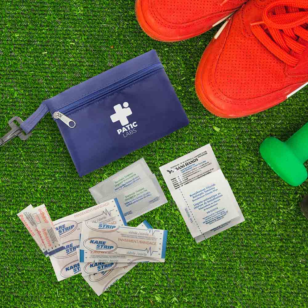 Blue PATIC LABS first aid pouch with bandages and wipes on green turf beside red sneakers.