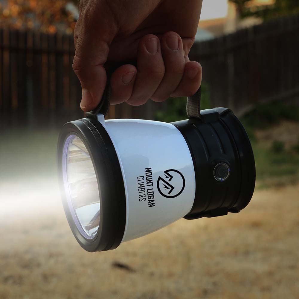 Handheld LED flashlight with black accents and a mountain logo, emitting a bright beam