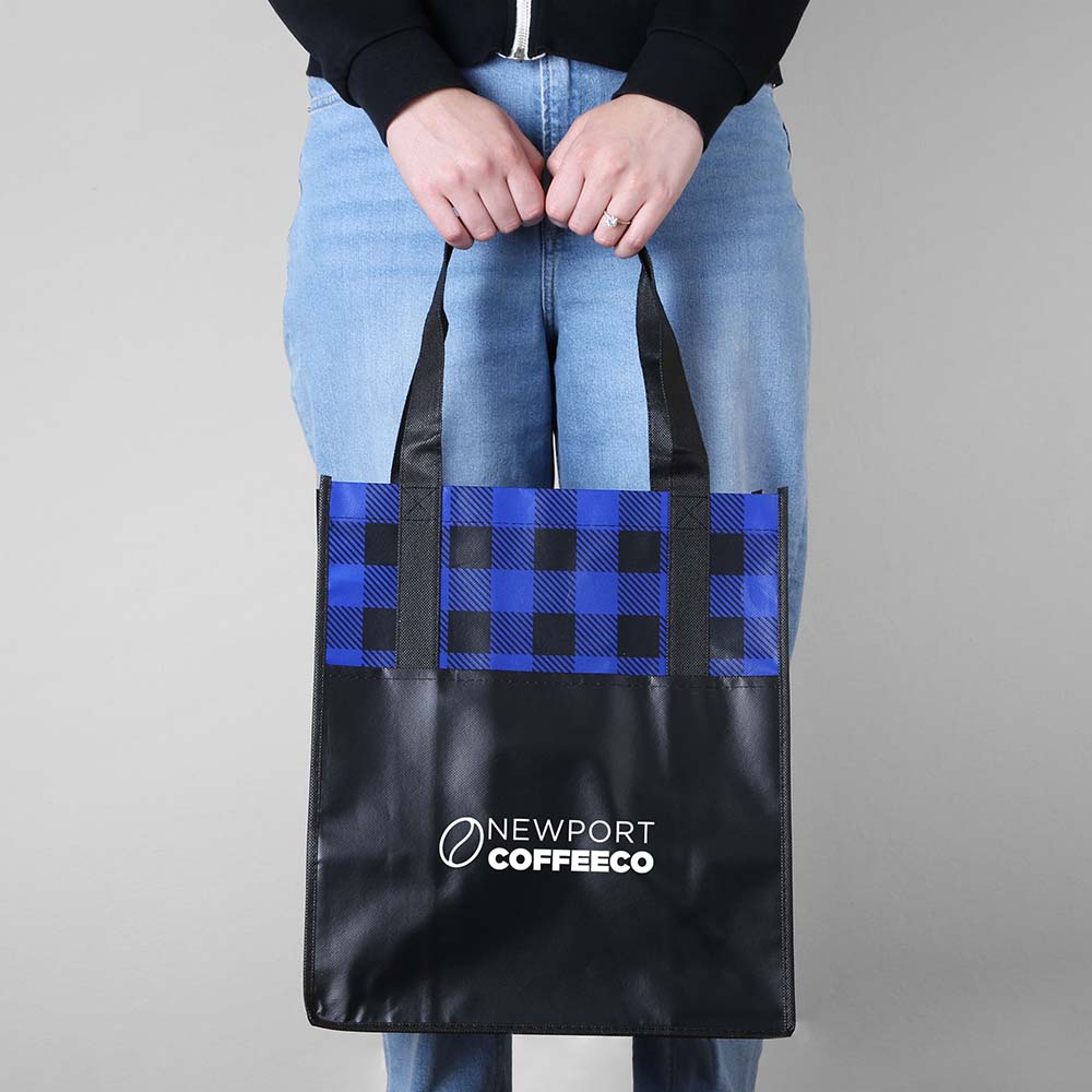 Person holding a blue and black plaid laminated tote bag with black handles and Newport Coffee Co. logo