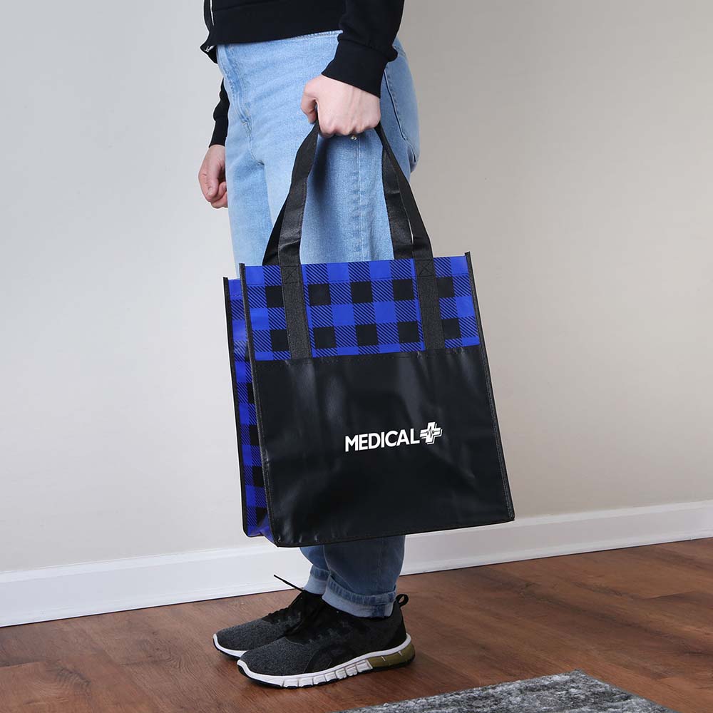 Side view of person holding a blue and black plaid laminated tote bag with MEDICAL+ logo