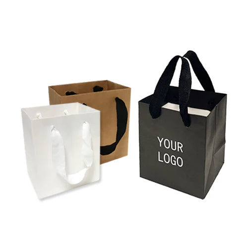 Small square gift bags in white, kraft, and black, each with thick ribbon handles and space for a custom logo.