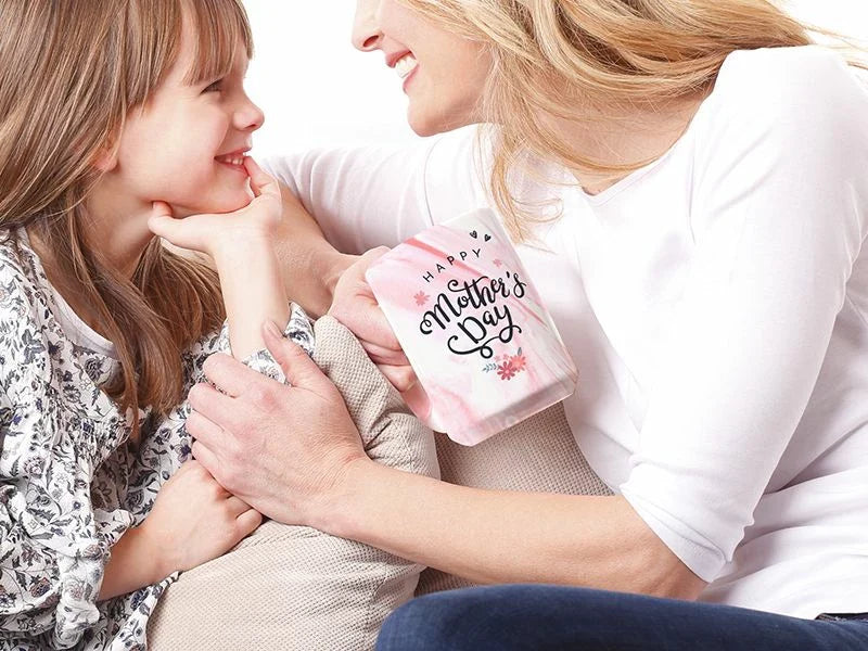 Mother and daughter smiling together, holding a pink marble ceramic mug with Happy Mother's Day design