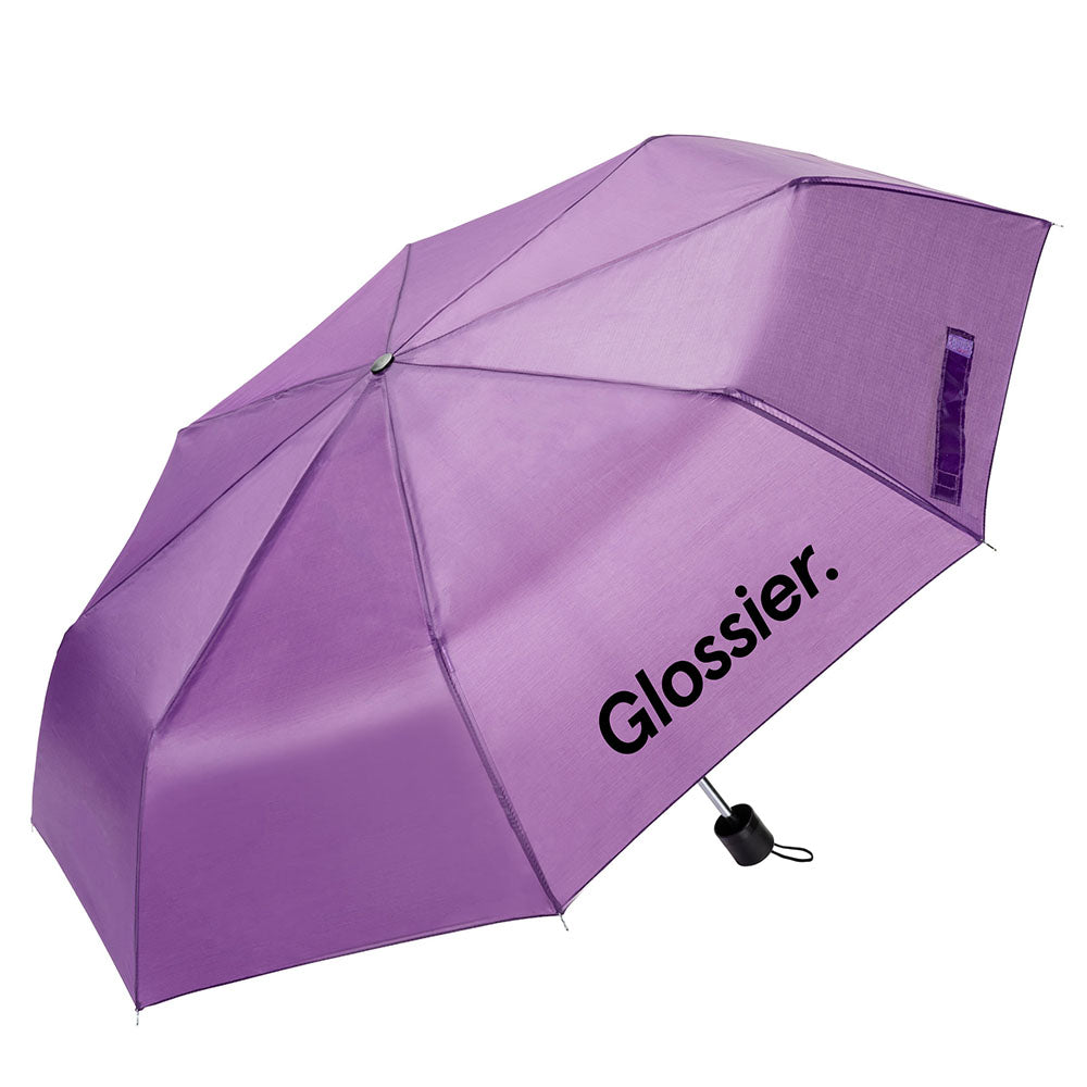Purple umbrella with the “Glossier.” logo printed in black on one panel, featuring a compact black handle and wrist strap.
