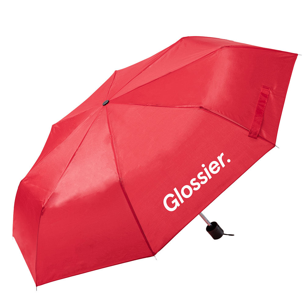 Red umbrella with the “Glossier.” logo printed in black on one panel, featuring a compact black handle and wrist strap.