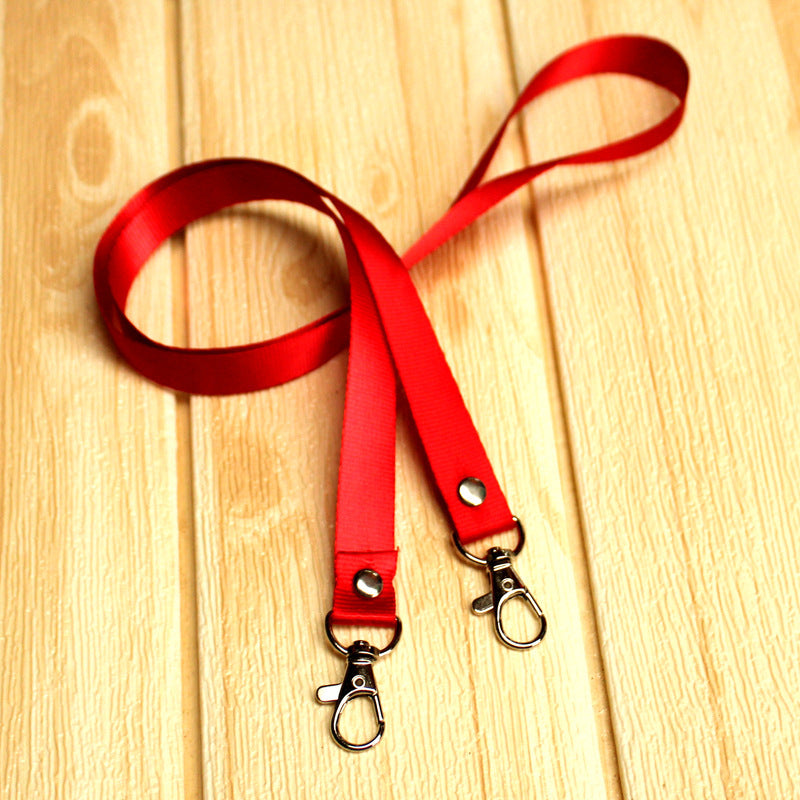 Vivid red nylon lanyard featuring two metal lobster clips and black rivets, displayed on a light wooden surface.