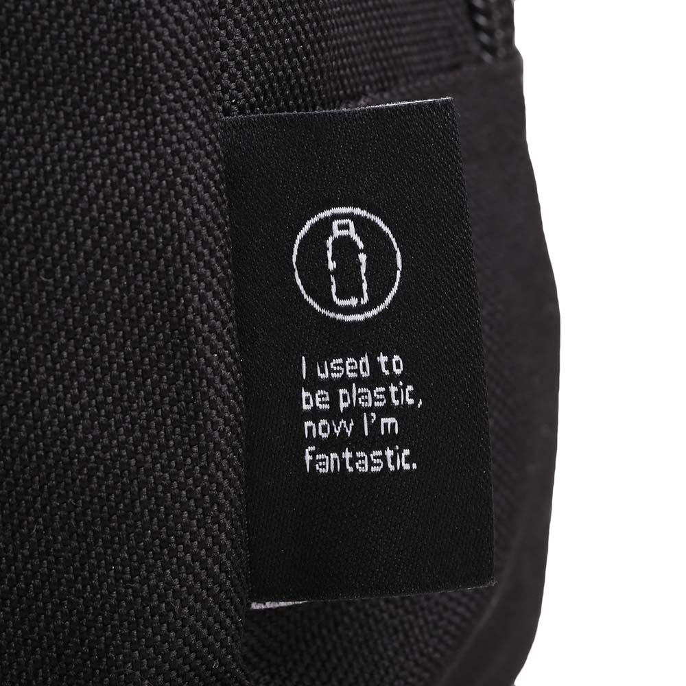 Close-up of eco-friendly fabric tag on a black toiletry bag with bottle icon and text: 'I used to be plastic, now I’m fantastic.'
