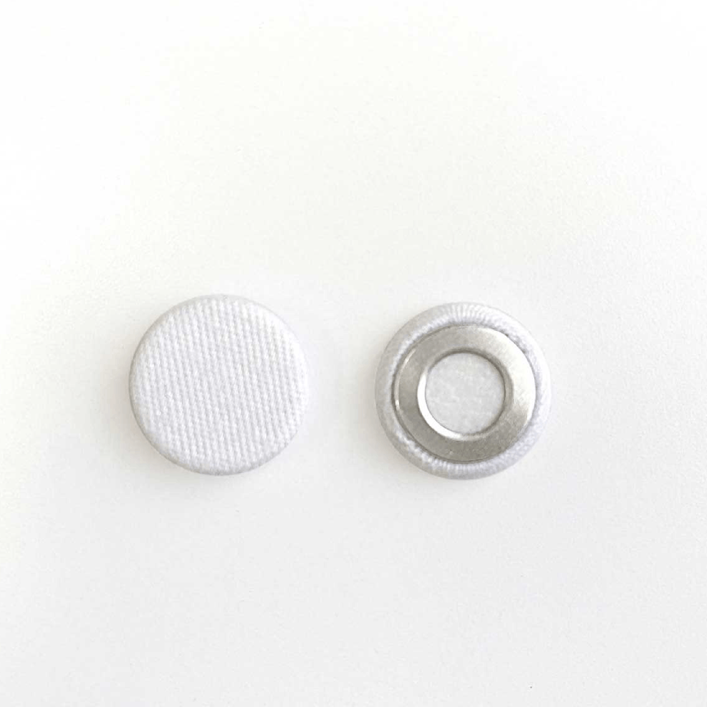 Close-up of two white fabric-covered snap buttons, front and back view, on a white background