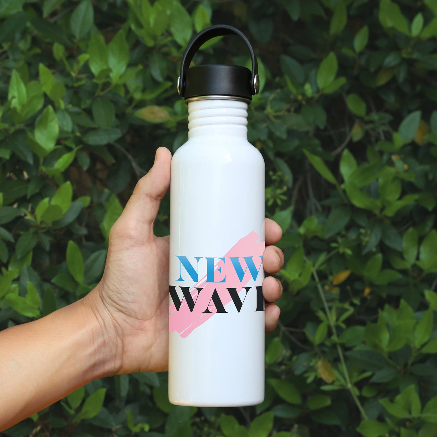 White bottle with 'NEW WAVE' design held in hand against leafy background