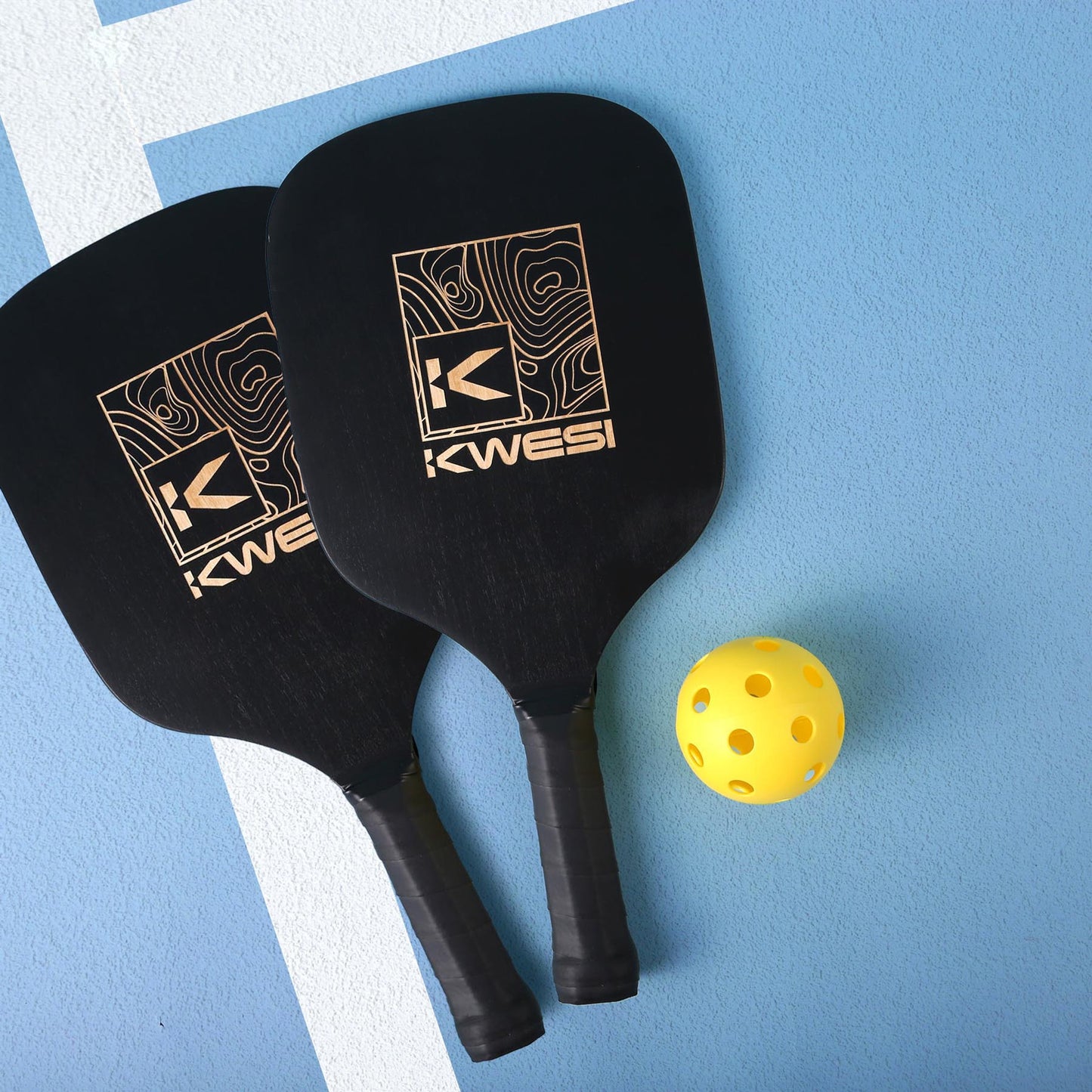 Two black pickleball paddles with logo and contour design resting on a blue court surface