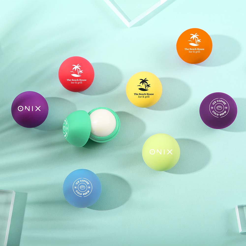 Assorted round lip balm containers in various colors with custom logos including ONIX, The Beach House, and OE Coffee; one container is open to show white balm inside.