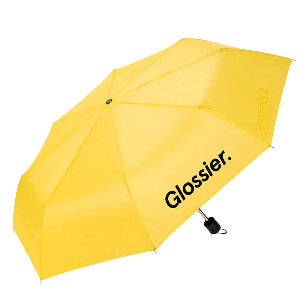 Yellow umbrella with the “Glossier.” logo printed in black on one panel, featuring a compact black handle and wrist strap.
