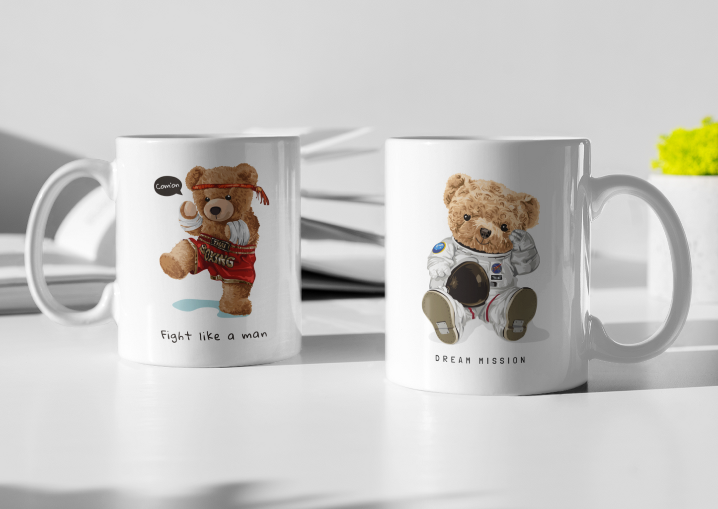 Two white mugs with cartoon teddy bear designs — one dressed as a boxer with the text "Fight like a man," and the other as an astronaut with the caption "Dream Mission."
