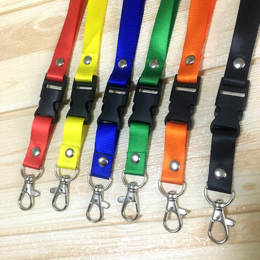 Assorted Custom Print Nylon Lanyards in red, yellow, blue, green, orange, and black, each featuring a detachable plastic buckle, metal lobster clip, and silver button snap, displayed on a light wooden background