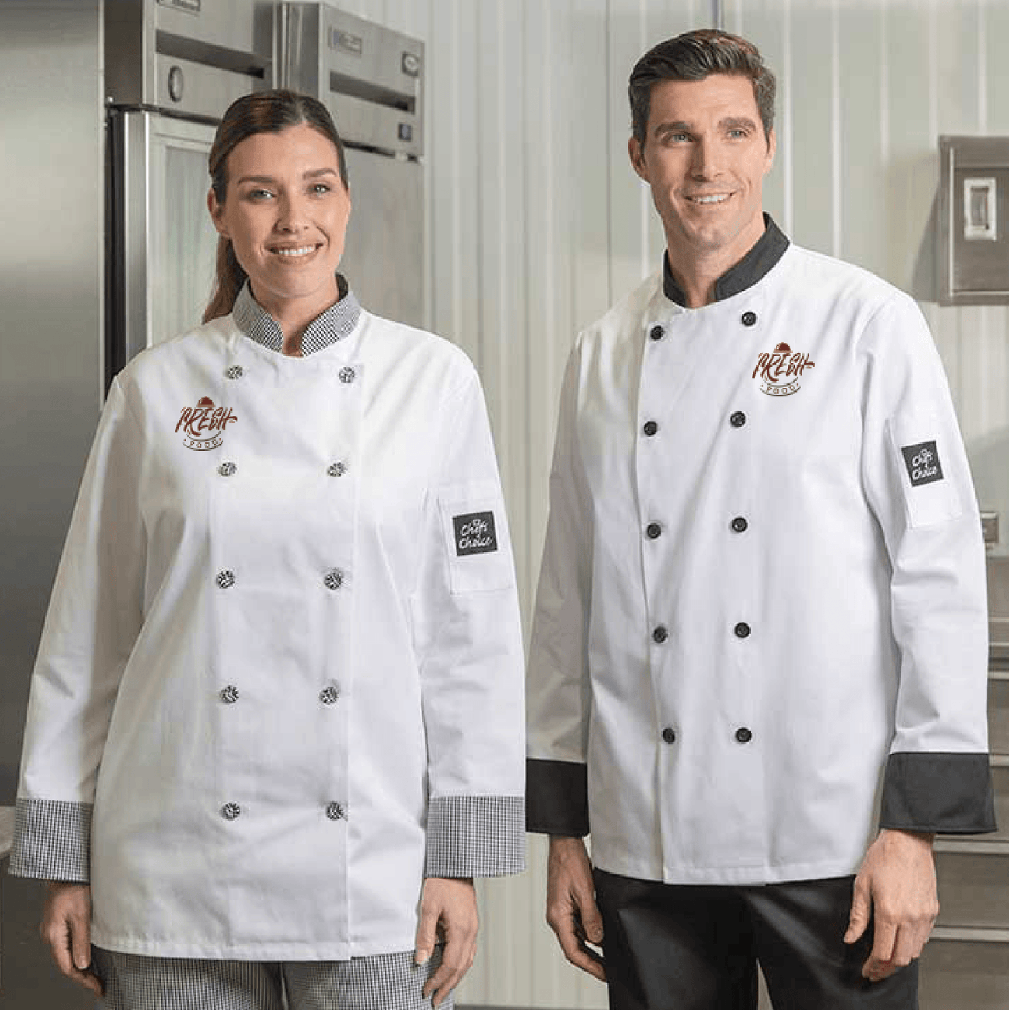 Two chefs wearing white chef coats with contrast trim and embroidered logos, standing in a commercial kitchen.