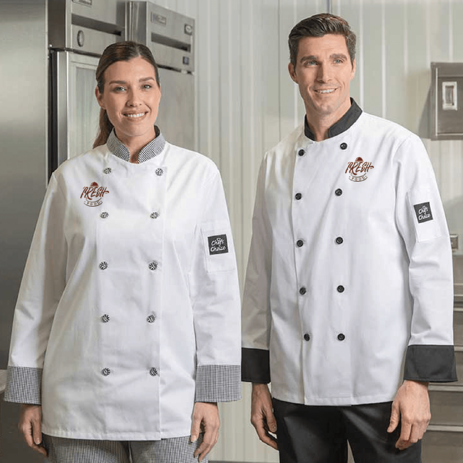 Two chefs wearing white chef coats with contrast trim and embroidered logos, standing in a commercial kitchen.