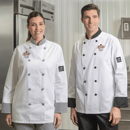 Two chefs wearing white chef coats with contrast trim and embroidered logos, standing in a commercial kitchen.
