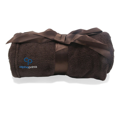 Rolled brown plush blanket tied with a satin ribbon and embroidered with the 'alphaprints' logo.