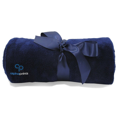 Rolled cabalt blue plush blanket tied with a satin ribbon and embroidered with the 'alphaprints' logo.