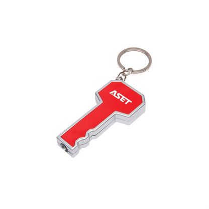 Key-shaped LED flashlight keychain in red and silver, featuring a bright white light at the tip and a customized 'ASET' logo printed on the head; includes a metal keyring for easy attachment.