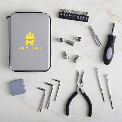 Flat lay of a compact gray tool kit with a yellow logo, surrounded by various tools including pliers, screwdrivers, Allen keys, socket heads, and a bit driver on a marble surface.