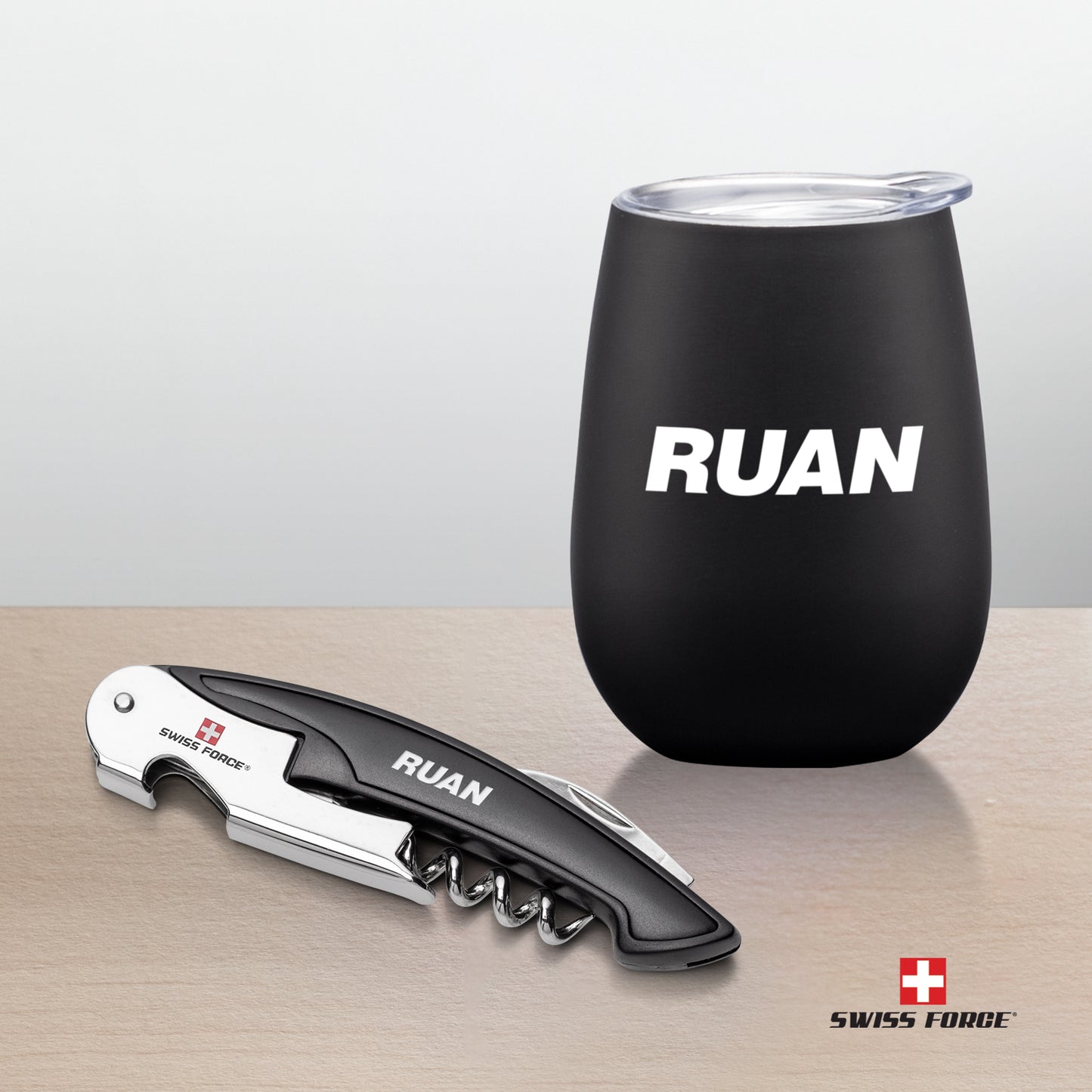 Swiss Force® Rosette Wine Gift Set with a matte black wine tumbler featuring a white 'RUAN' logo and a matching corkscrew bottle opener with engraved branding, displayed on a light wooden surface.
