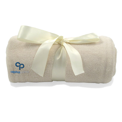 Rolled vanilla beige plush blanket tied with a satin ribbon and embroidered with the 'alphaprints' logo.