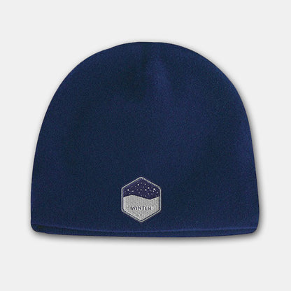 Navy blue deluxe fleece beanie with a hexagon-shaped embroidered patch featuring a snowy night design on the front.