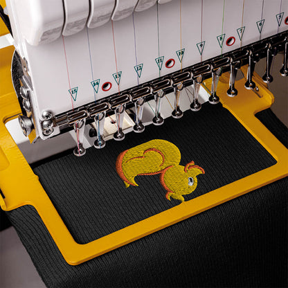 Close-up of an embroidery machine stitching a yellow and orange duck design onto a black knit fabric, secured in a yellow embroidery frame.