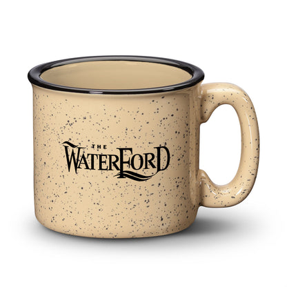 Sand ceramic campfire mug with a speckled finish, black rim, and “The Waterford” logo in bold print.
