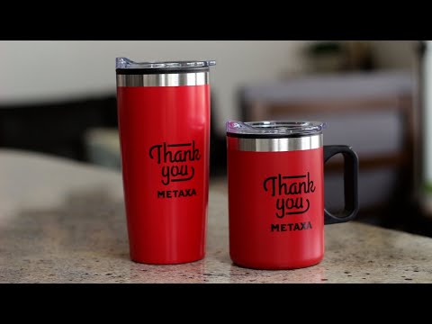 Lou Asador Mug & Tumbler Gift Set in red with black 'Thank you METAXA' print, featuring a tall tumbler and a handle mug, both with clear lids, displayed on a kitchen counter.