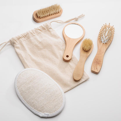 Natural spa kit with beige drawstring pouch, wooden-handled mirror, brushes, comb, and loofah pad — no logo imprint visible.