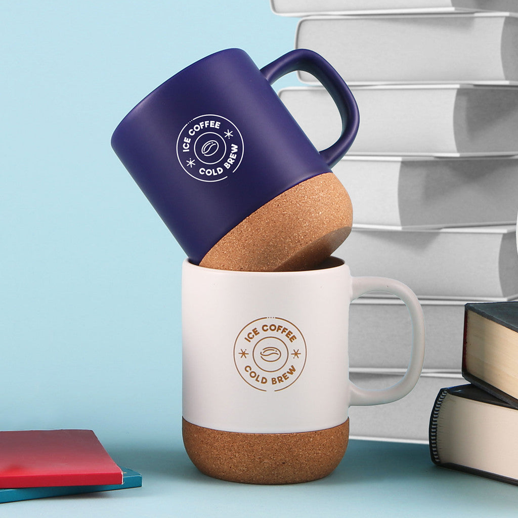 Stacked ceramic mugs with natural cork bottoms, one in navy and one in white, both featuring 'Ice Coffee Cold Brew' logos.